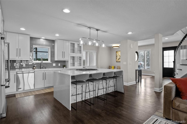 kitchen with decorative backsplash, appliances with stainless steel finishes, decorative light fixtures, white cabinets, and a center island