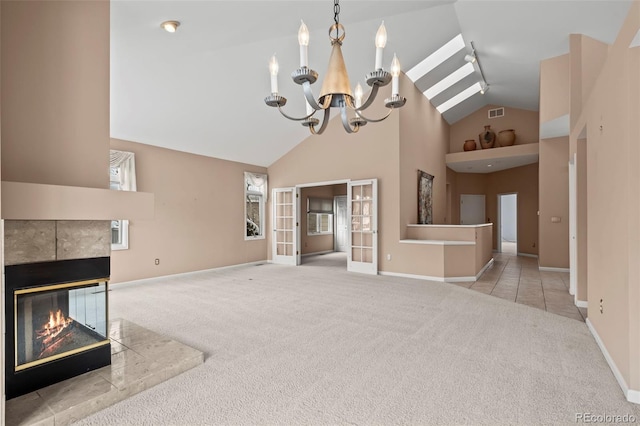 unfurnished living room featuring high vaulted ceiling, a fireplace, a notable chandelier, light carpet, and french doors