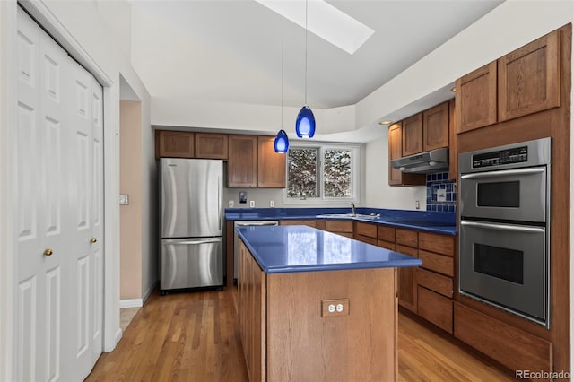 kitchen with pendant lighting, appliances with stainless steel finishes, a skylight, light hardwood / wood-style floors, and a kitchen island