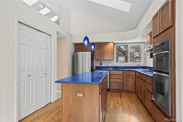 kitchen with lofted ceiling with skylight, stainless steel appliances, a kitchen island, decorative light fixtures, and light wood-type flooring