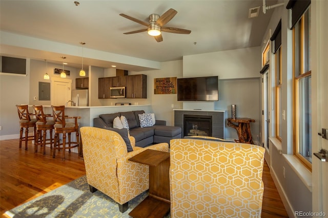 living room featuring electric panel, a ceiling fan, a fireplace, dark wood finished floors, and baseboards