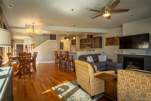 living room featuring visible vents, wood finished floors, a fireplace, baseboards, and ceiling fan with notable chandelier