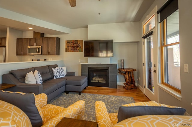 living room featuring recessed lighting, ceiling fan, a glass covered fireplace, and wood finished floors