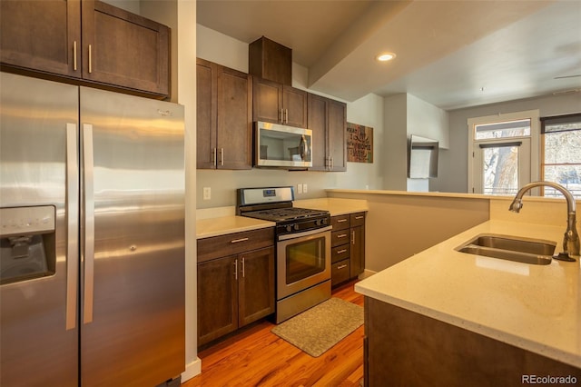 kitchen with dark brown cabinetry, a sink, light wood-style floors, stainless steel appliances, and recessed lighting
