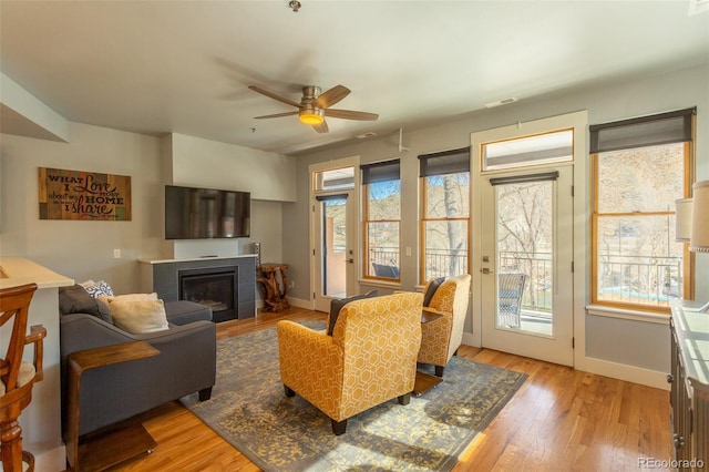 living area featuring visible vents, a glass covered fireplace, baseboards, ceiling fan, and light wood finished floors