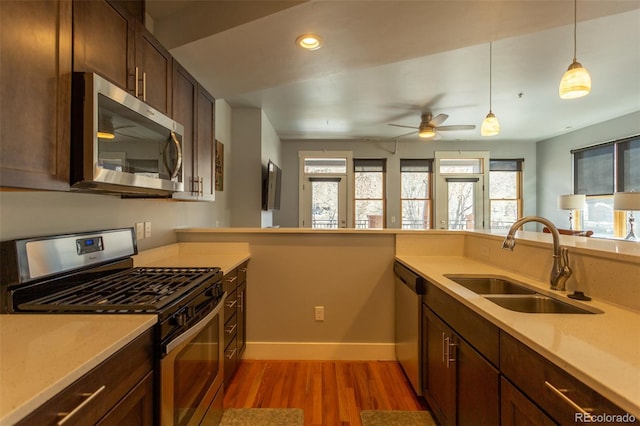kitchen featuring ceiling fan, a sink, light countertops, stainless steel appliances, and light wood-style flooring