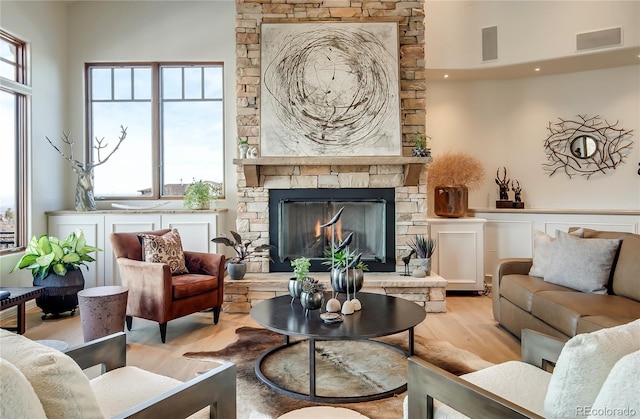 living area featuring plenty of natural light, a stone fireplace, light wood-type flooring, and visible vents