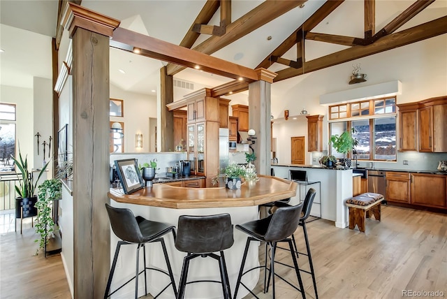 kitchen featuring brown cabinets, backsplash, a peninsula, light wood-type flooring, and beam ceiling