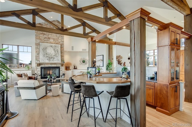 kitchen featuring light wood-style flooring, brown cabinets, a stone fireplace, and a kitchen breakfast bar