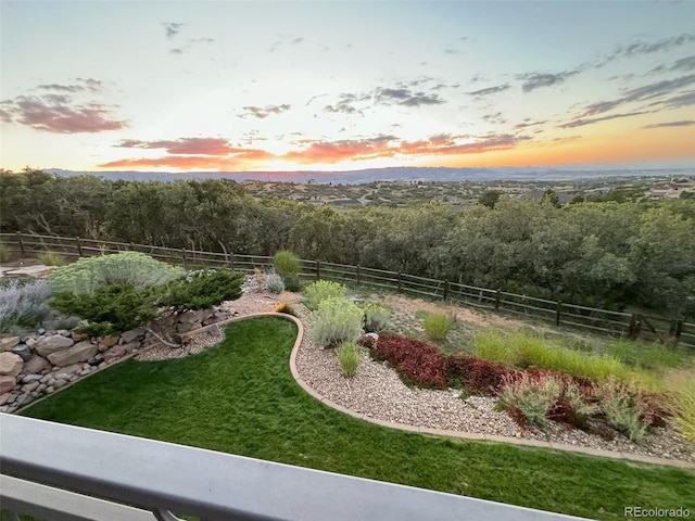 yard at dusk featuring a forest view and fence