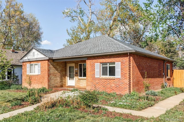 view of front facade with brick siding, a shingled roof, and fence