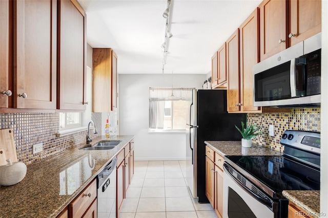 kitchen with stainless steel appliances, a sink, track lighting, baseboards, and dark stone counters