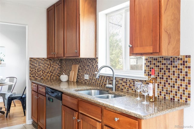 kitchen with stainless steel dishwasher, a sink, backsplash, light stone countertops, and healthy amount of natural light
