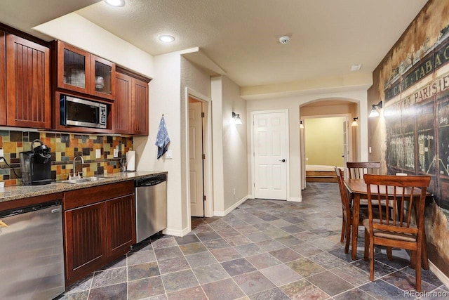 14200 W 86th Pl, Arvada, CO 80005 - kitchen with stainless steel appliances, a sink, arched walkways, baseboards, and glass insert cabinets