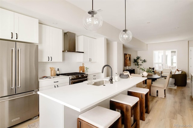 8260 E 36th Ave Unit 30, Denver, CO 80238 - kitchen with appliances with stainless steel finishes, wall chimney range hood, a sink, light wood-style floors, and an island with sink