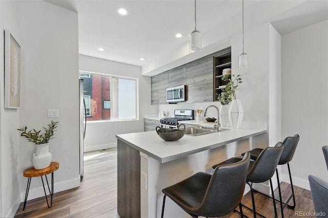 kitchen featuring a kitchen bar, a sink, open shelves, appliances with stainless steel finishes, and a peninsula