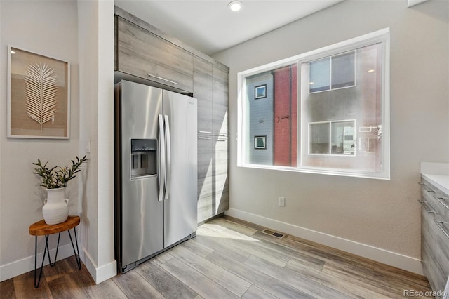 kitchen featuring visible vents, light wood-style floors, stainless steel fridge, and baseboards