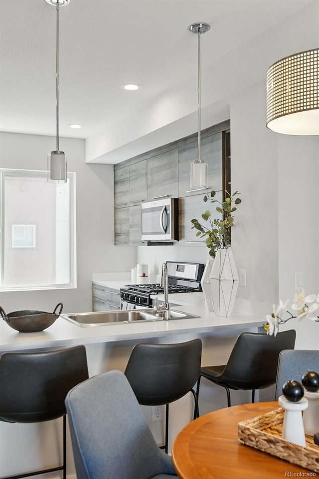 kitchen featuring a breakfast bar area, a peninsula, stainless steel appliances, hanging light fixtures, and light countertops