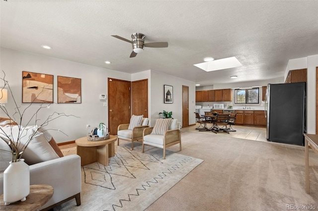 living room with a skylight, light colored carpet, ceiling fan, a textured ceiling, and recessed lighting