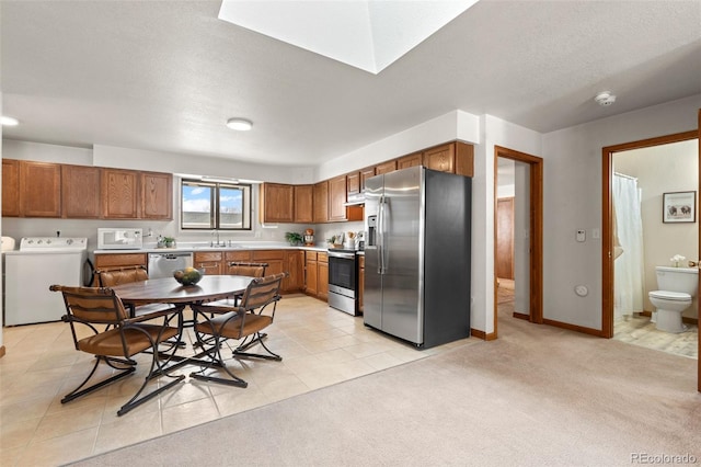 kitchen with appliances with stainless steel finishes, brown cabinetry, light countertops, and independent washer and dryer