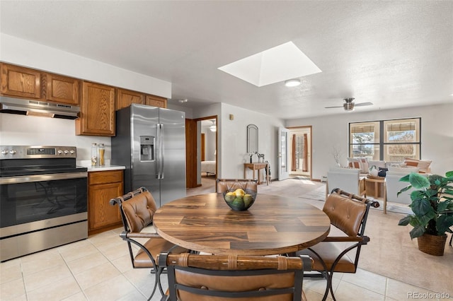 dining space featuring a skylight, light tile patterned floors, a ceiling fan, and a textured ceiling