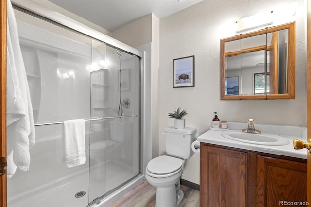 bathroom featuring toilet, a stall shower, wood finished floors, and vanity