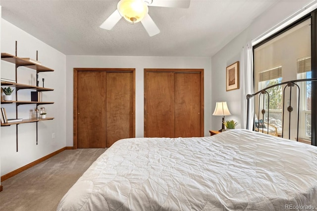 bedroom with two closets, light colored carpet, a ceiling fan, a textured ceiling, and baseboards