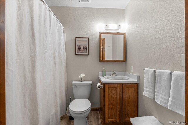 bathroom with visible vents, a textured wall, toilet, vanity, and wood finished floors