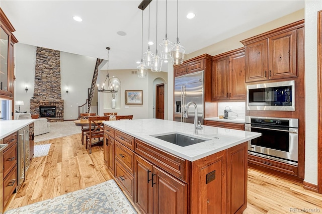 10459 Rivington Ct, Lone Tree, CO 80124 - kitchen with appliances with stainless steel finishes, a sink, light wood-style flooring, a stone fireplace, and brown cabinets