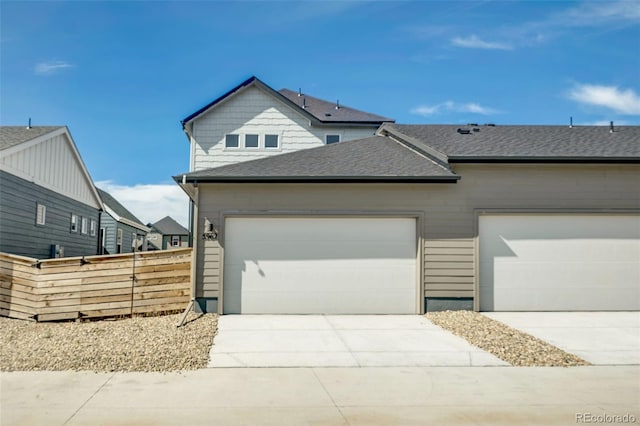 view of front of house with driveway, roof with shingles, fence, and a garage