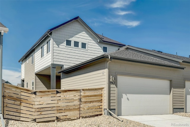 view of side of home with fence, concrete driveway, roof with shingles, and a garage