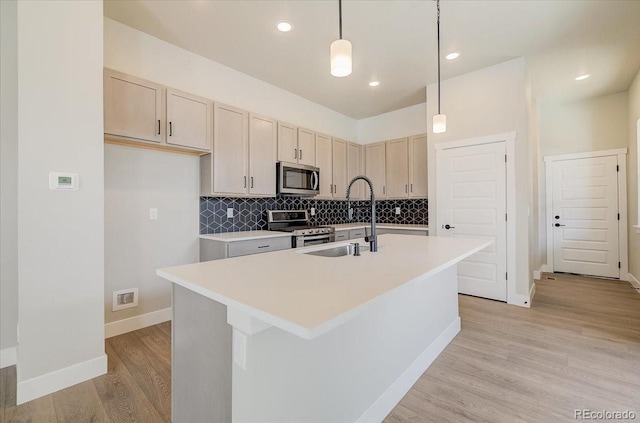 kitchen with appliances with stainless steel finishes, a center island with sink, light wood-type flooring, light countertops, and tasteful backsplash