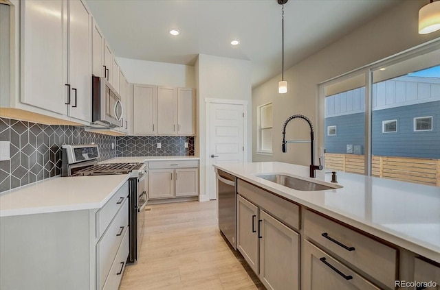kitchen featuring appliances with stainless steel finishes, a sink, light countertops, light wood-type flooring, and hanging light fixtures