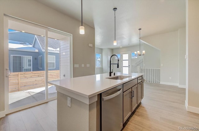 kitchen featuring a sink, stainless steel dishwasher, light wood-style flooring, pendant lighting, and baseboards