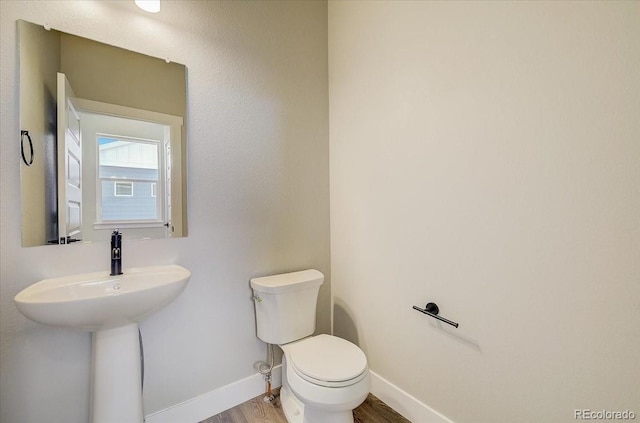 half bathroom featuring wood finished floors, toilet, and baseboards