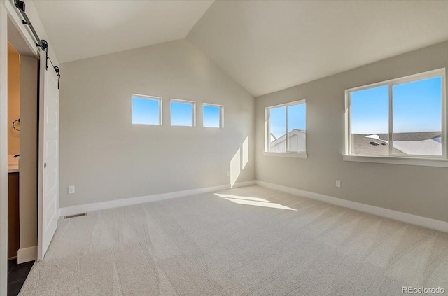 unfurnished bedroom with a barn door, carpet flooring, baseboards, multiple windows, and lofted ceiling