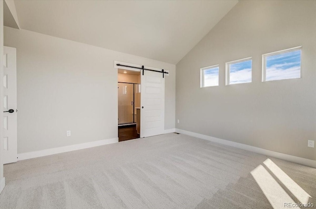 unfurnished bedroom with a barn door, carpet flooring, baseboards, high vaulted ceiling, and connected bathroom