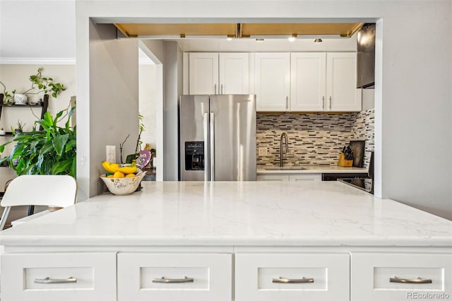 kitchen featuring tasteful backsplash, stainless steel refrigerator with ice dispenser, a sink, and white cabinetry