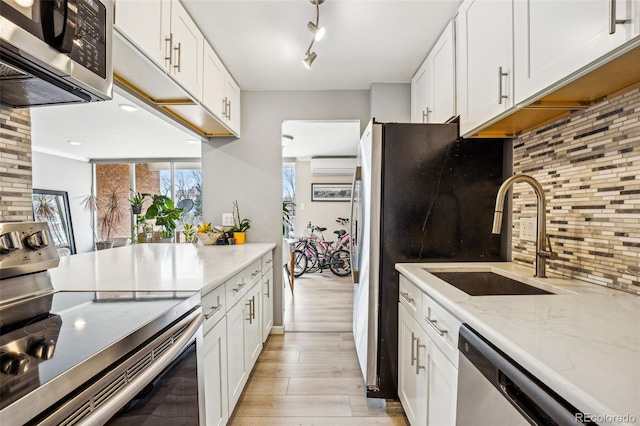 kitchen featuring appliances with stainless steel finishes, an AC wall unit, white cabinets, a sink, and light wood-type flooring