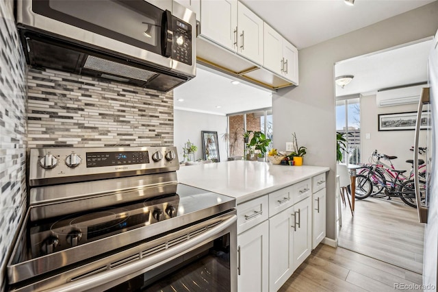 kitchen featuring a wall unit AC, appliances with stainless steel finishes, light countertops, light wood-style floors, and white cabinetry