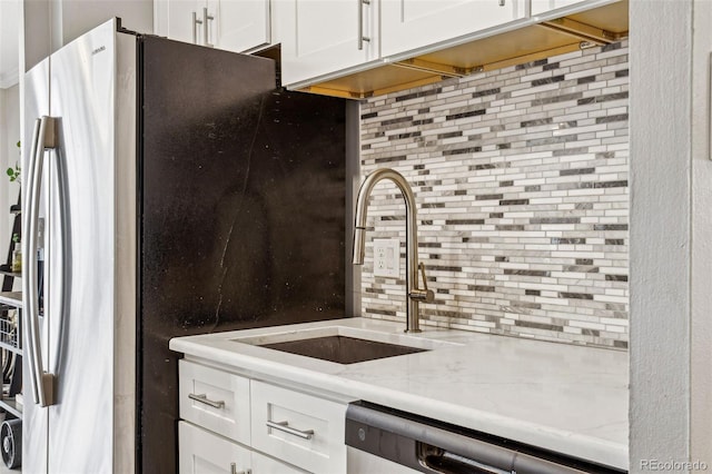 kitchen featuring dishwashing machine, light stone counters, a sink, white cabinetry, and tasteful backsplash