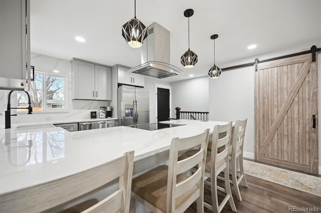 kitchen featuring kitchen peninsula, island range hood, stainless steel appliances, gray cabinets, and a barn door