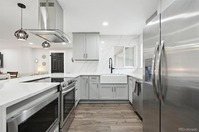 kitchen featuring wall chimney exhaust hood, hanging light fixtures, stainless steel appliances, gray cabinetry, and sink