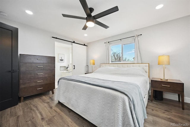 bedroom with ceiling fan, dark wood-type flooring, and a barn door