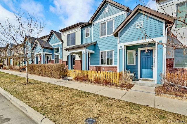 townhome / multi-family property with a fenced front yard, a residential view, brick siding, and a front yard