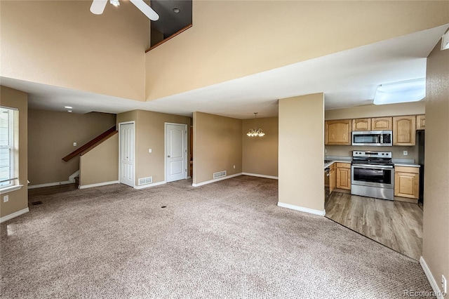1419 Red Mountain Dr Unit 126, Longmont, CO 80504 - unfurnished living room with light colored carpet, stairs, ceiling fan, a chandelier, and a towering ceiling