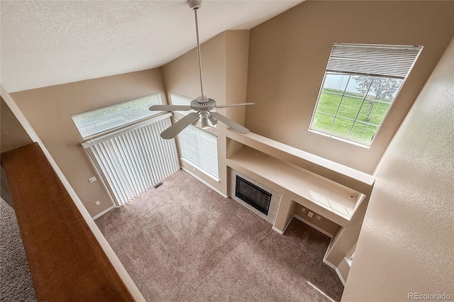 1419 Red Mountain Dr Unit 126, Longmont, CO 80504 - unfurnished living room with a ceiling fan, carpet, lofted ceiling, a textured ceiling, and a glass covered fireplace