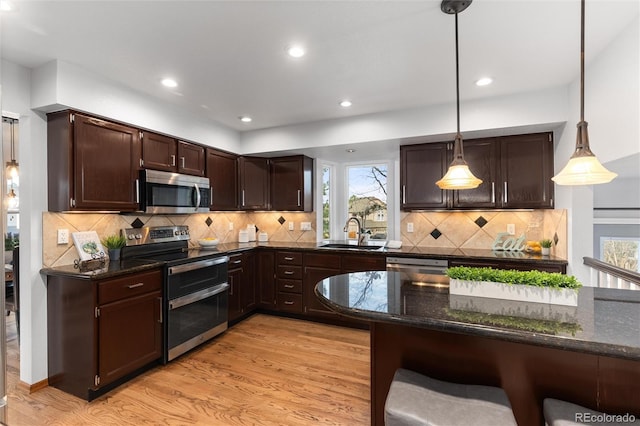 7636 S Allison Ct, Littleton, CO 80128 - kitchen with appliances with stainless steel finishes, a breakfast bar area, light wood-type flooring, dark brown cabinetry, and dark stone countertops