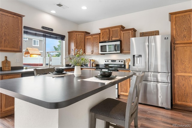 5536 Kirk St, Denver, CO 80249 - kitchen featuring stainless steel appliances, dark countertops, brown cabinetry, a breakfast bar area, and dark wood-type flooring