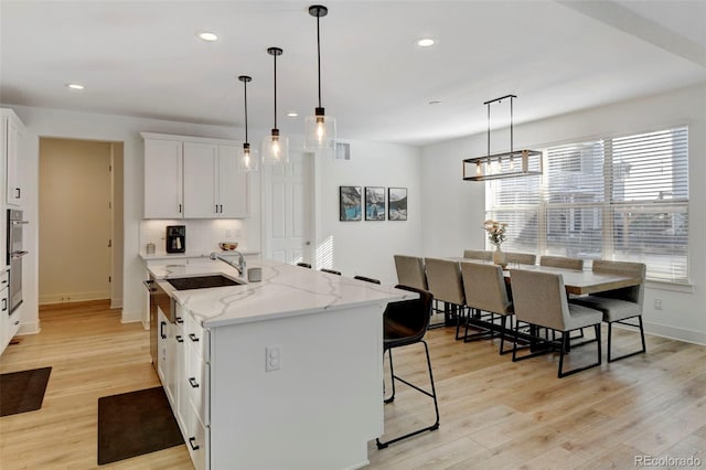 kitchen with a kitchen island with sink, white cabinets, light stone counters, and light hardwood / wood-style floors